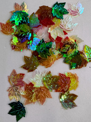 Iridescent plastic leaf shapes scattered on a white surface.