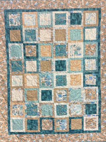 Peaceful quilt with squares of teal, tan, and floral patterns.