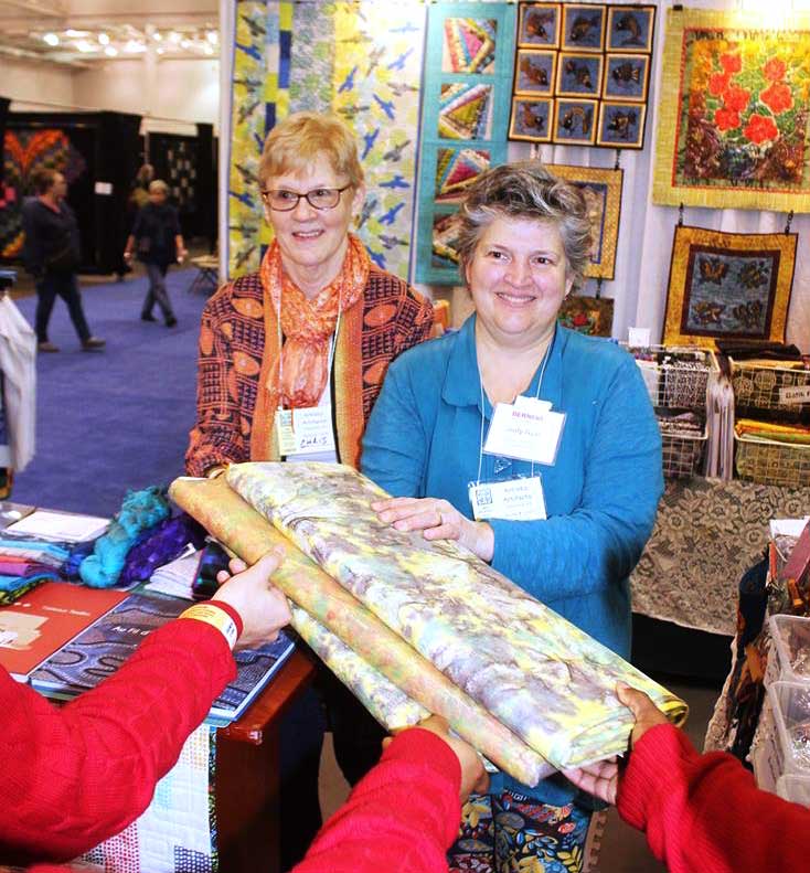 Christine Vinh and Artistic Artifacts owner Judy Gula present Roy Mitchell's quilting students with three bolts of Indonesian-made material for their classroom.