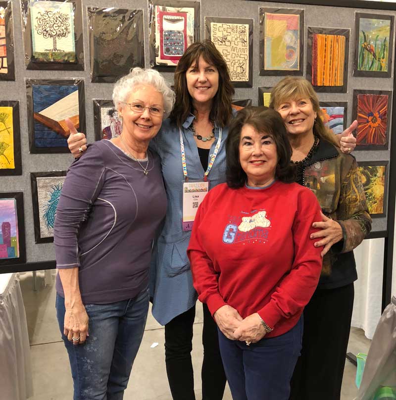 Lisa Ellis poses with QuiltCon attendees in front of the SAQA Trunk Show exhibit