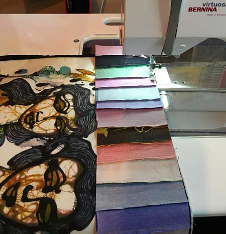 Sewing a chain-pieced silk border to the batik quilt panel.