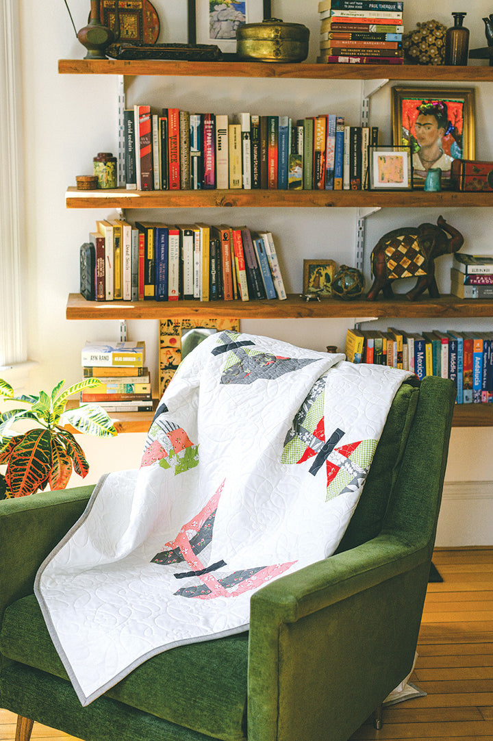 Green armchair with a quilt, bookshelves in the background.