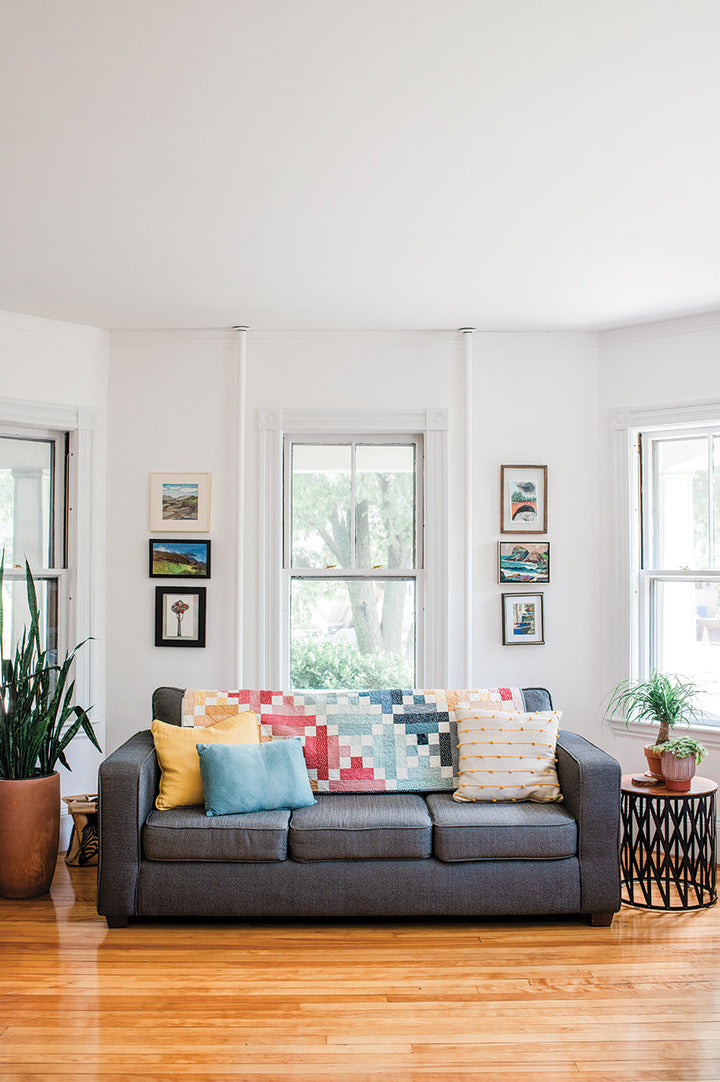 Gray sofa with colorful quilt and pillows.