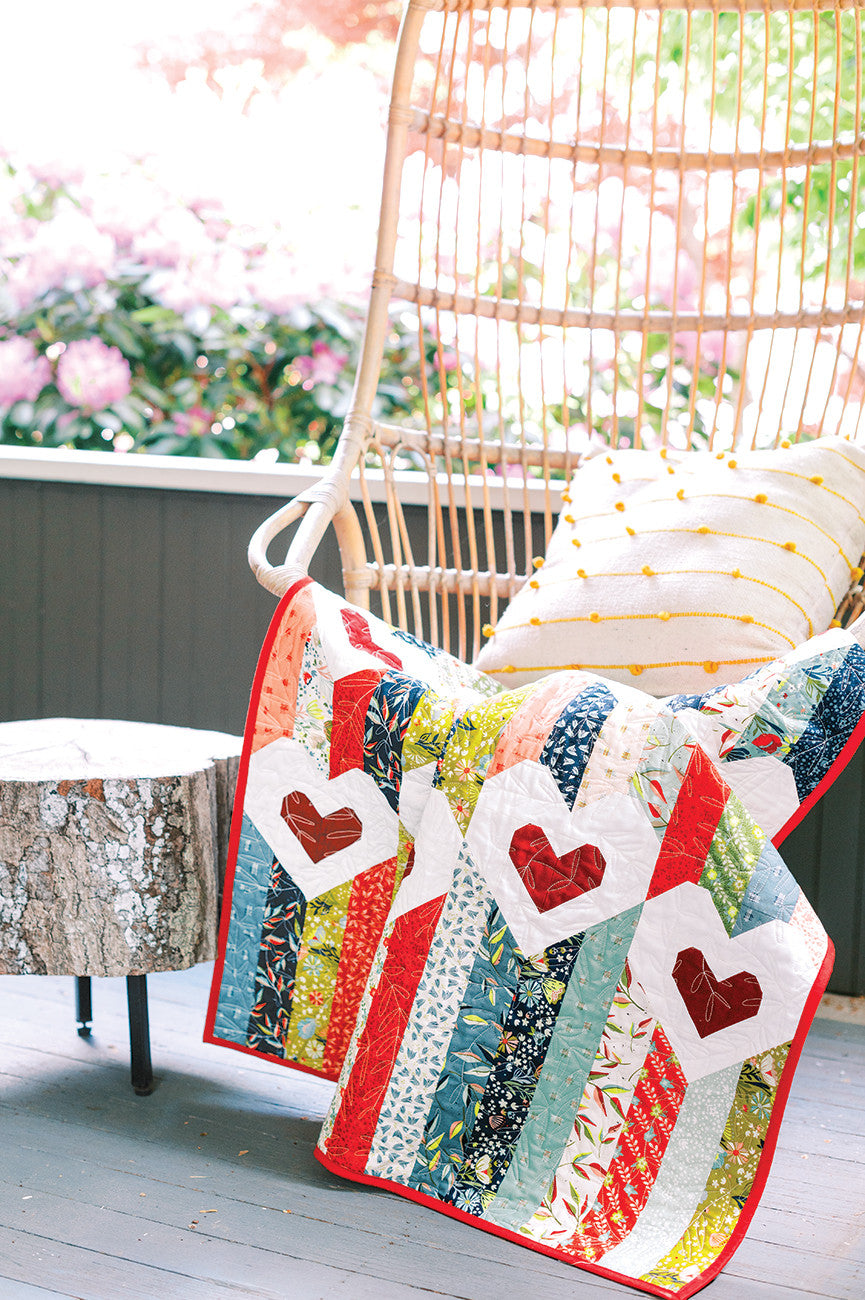 Quilt with heart appliqués on wicker chair with pillow.