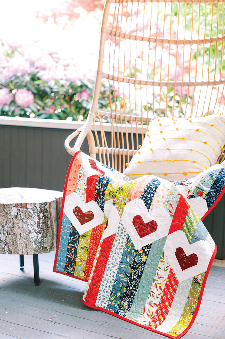 Quilt with heart appliqués on wicker chair with pillow.