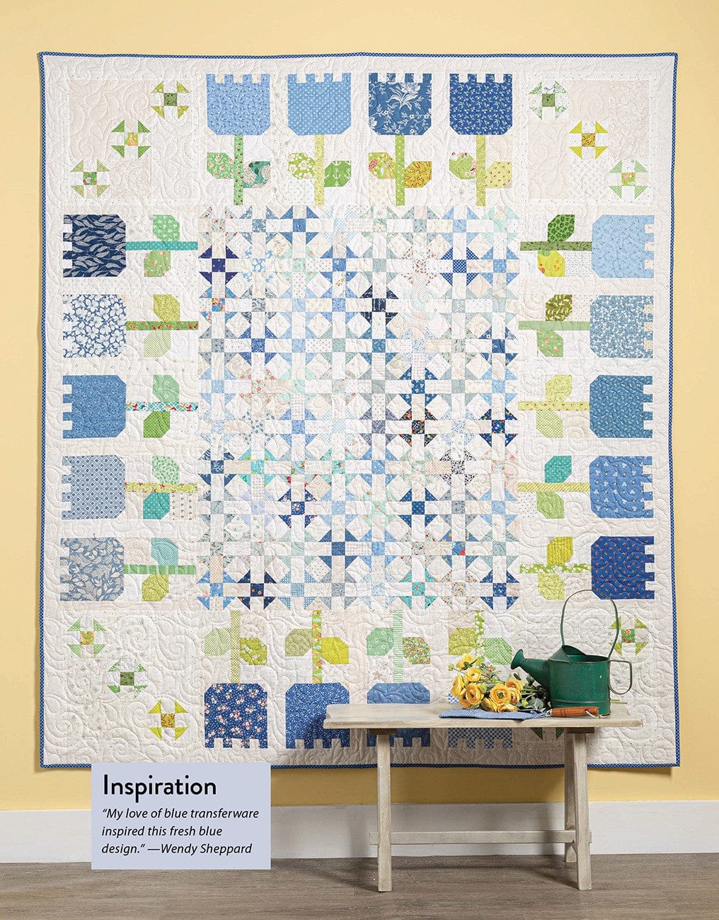 Quilt with blue flower pattern, bench, and small accessories.