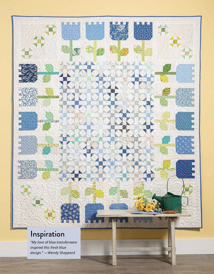 Quilt with blue flower pattern, bench, and small accessories.