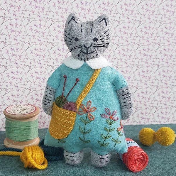 Stuffed cat doll in blue dress with yarn bag and sewing supplies.