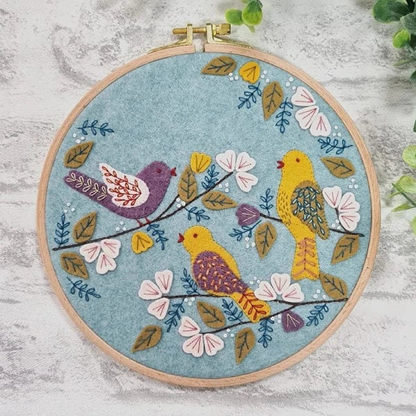 Embroidery hoop with three birds on branches and flowers.