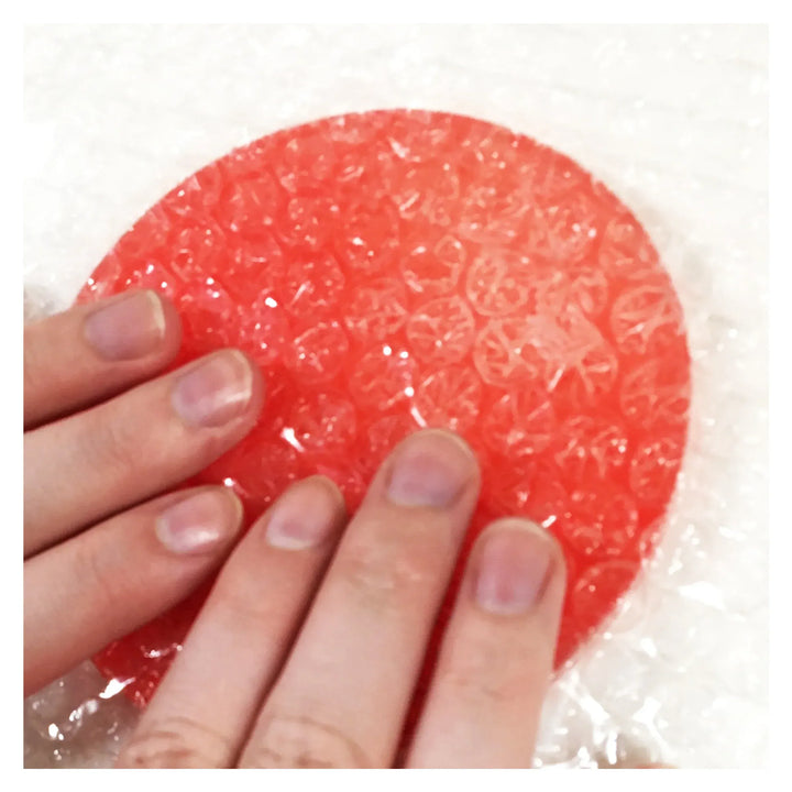 Hands holding red object wrapped in bubble wrap