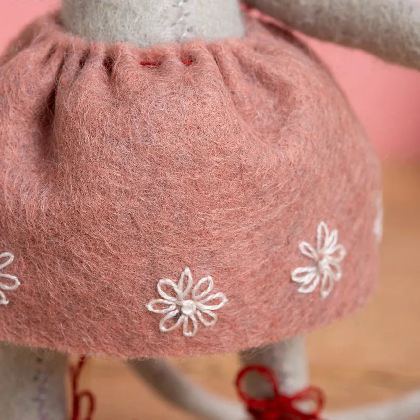 Close-up of a doll wearing a pink skirt with white flower embroidery.
