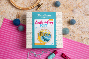 Embroidery kit box with supplies on a patterned surface.