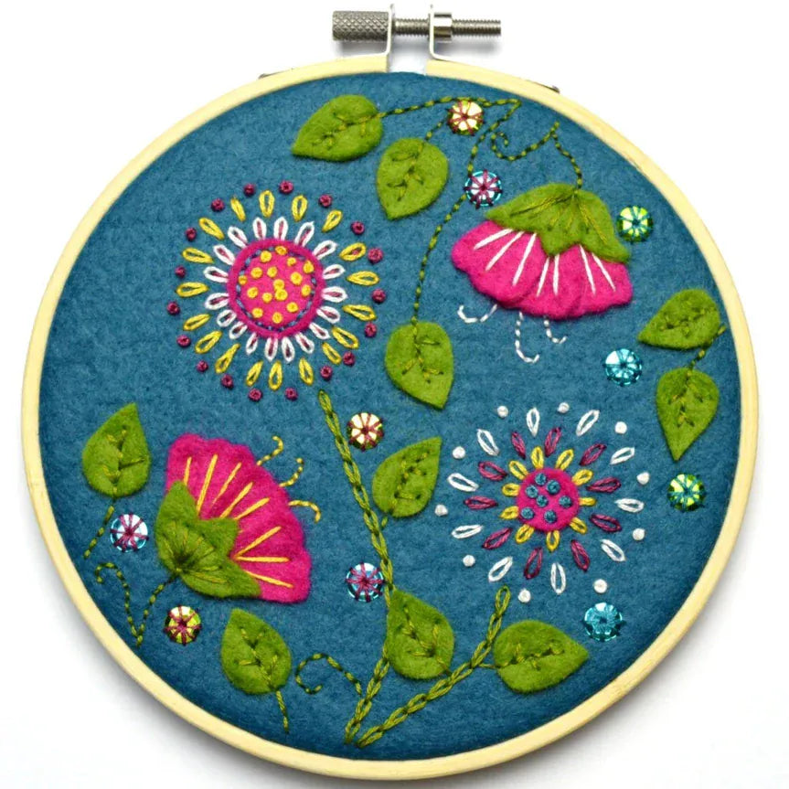 Embroidery hoop with pink and yellow flowers and green leaves.
