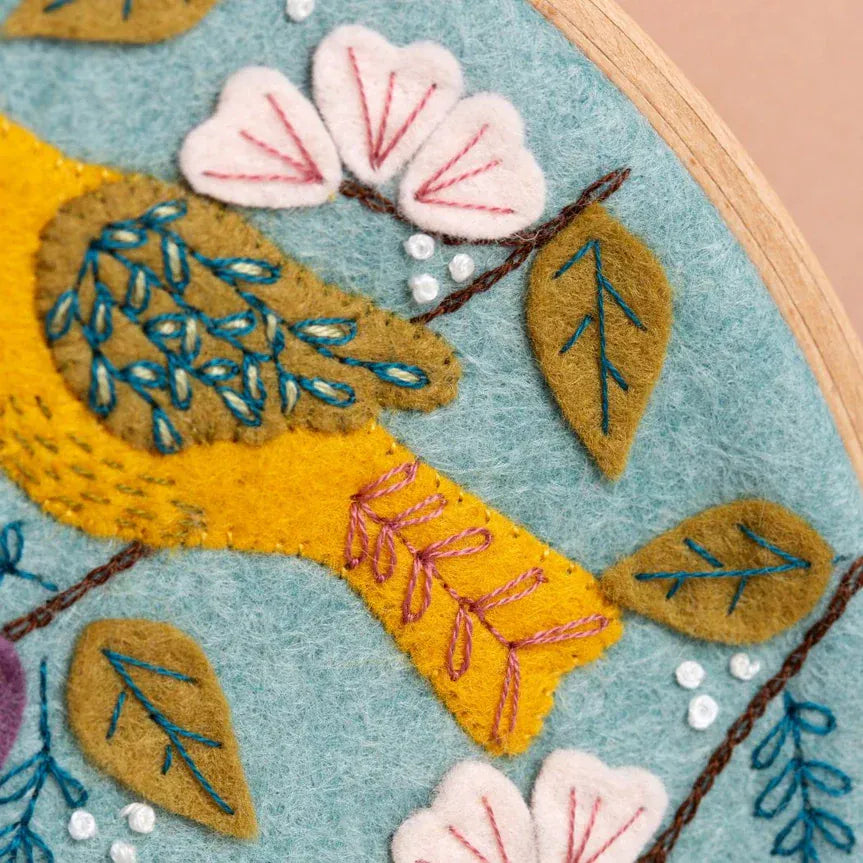 Embroidered bird with flowers and leaves on blue fabric.