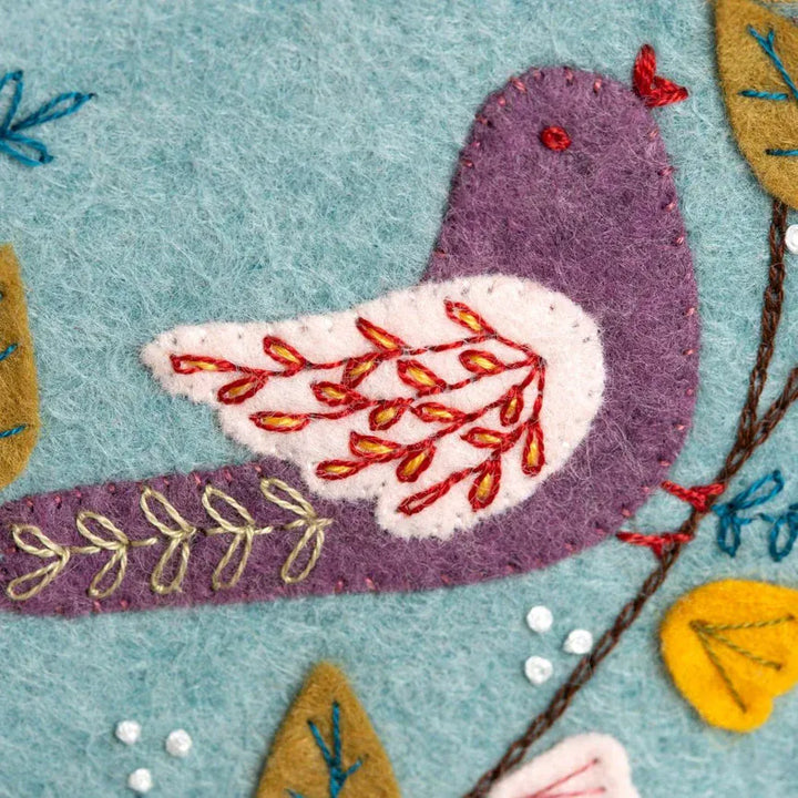 Purple felt bird with embroidered wing on blue background.