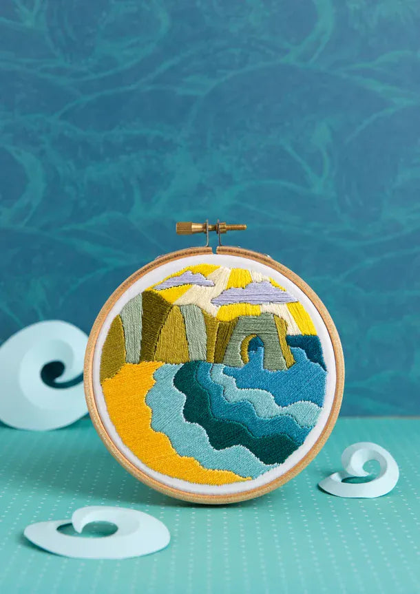 Embroidery of a coastal scene with beach, cliffs, and ocean.