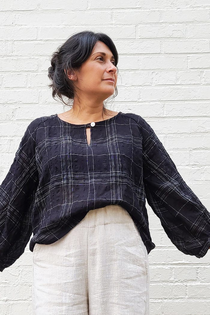 Woman wearing a black plaid top and light pants.