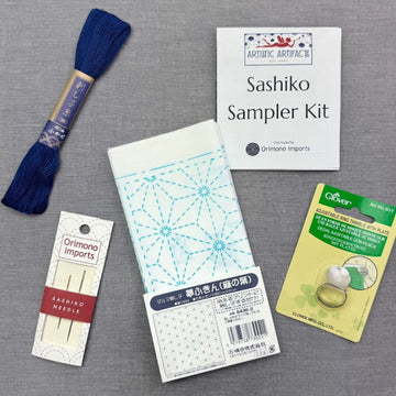 Sashiko sampler kit, thread, needles, and thimble on gray surface.