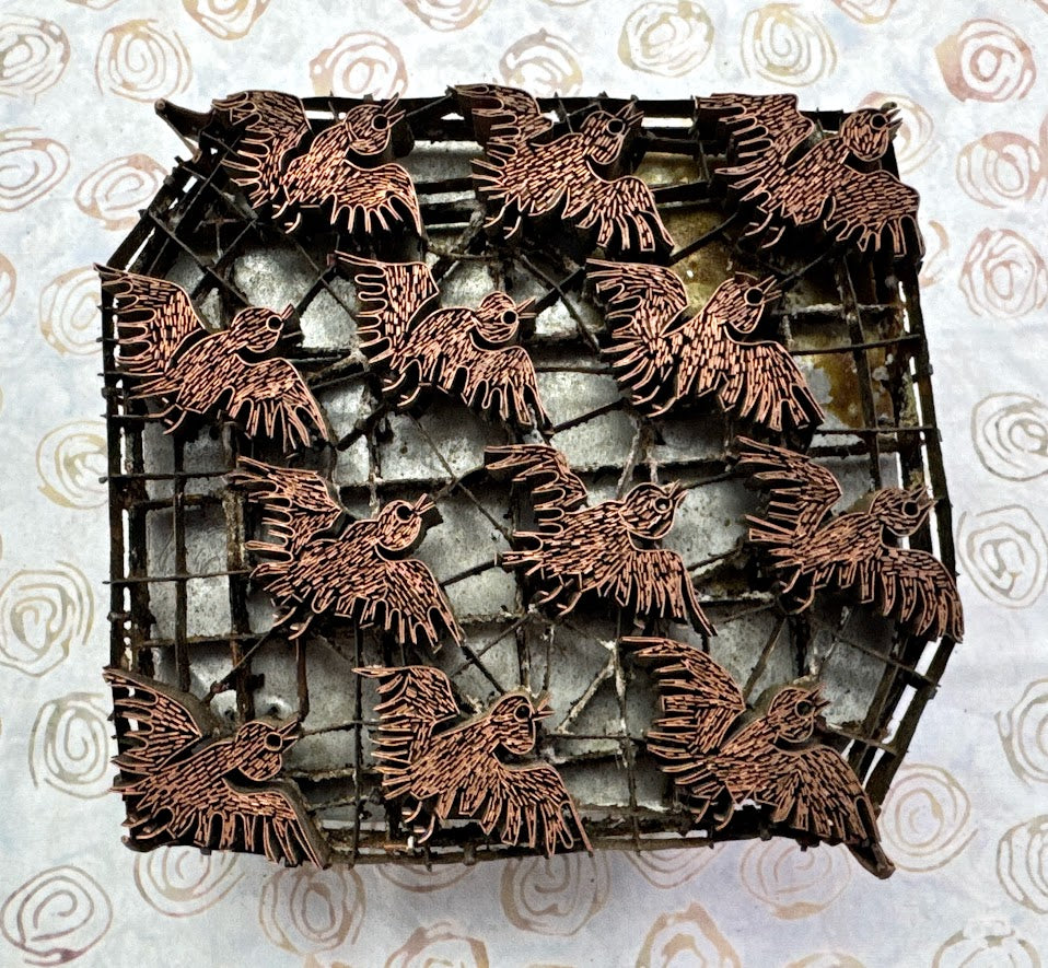 Bronze bird figurines on a metal grid against a patterned background