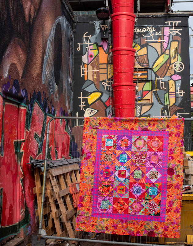 KF-QiL Economy Redweb art quilt with colorful urban backdrop.