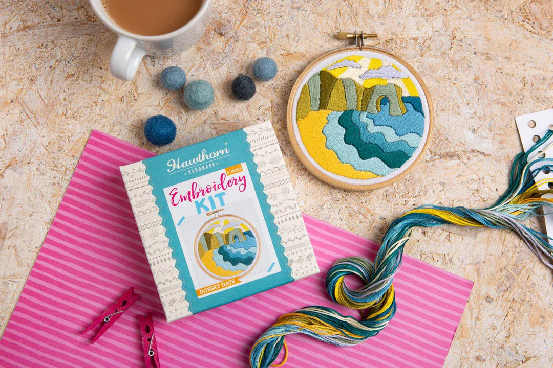 Embroidery kit, hoop art, yarn, and coffee cup on a table.